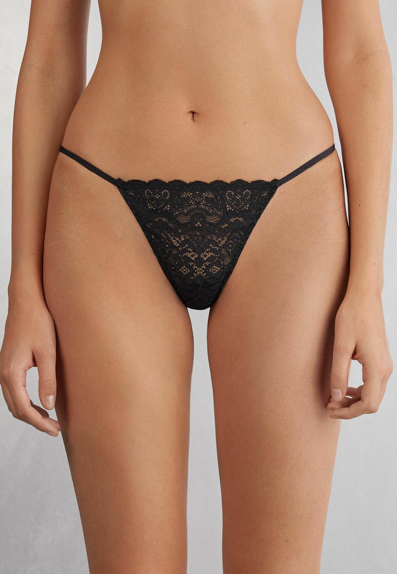 Zwarte kanten string met een geschulpte rand en een ingewikkeld hartpatroon, met dunne bandjes voor minimale bedekking.