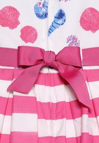 Detalle del vestido con rayas horizontales en rosa y blanco, un gran lazo texturizado en rosa en la cintura y un patrón de conchas en azul y rosa en la parte superior.