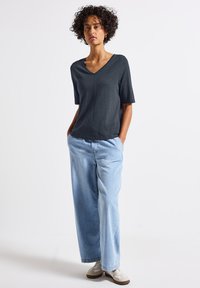 Ciemnoszara bluzka z dekoltem w serek i krótkim rękawem, zestawiona z luźnymi jasnoniebieskimi dżinsami i beżowymi sneakersami, charakteryzująca się luźnym krojem i miękką teksturą tkaniny.