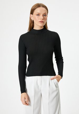 Haut à col roulé noir à côtes avec des manches longues, design ajusté et finition texturée, associé à un pantalon blanc taille haute.