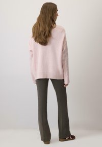 Pulover tricotat roz, cu croială lejeră și tiv cu zimți, asortat cu pantaloni evazați de culoare verde măslin. Textură moale cu detalii de tricotaj cu cabluri pe mâneci.