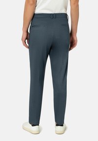 Donkerblauwe op maat gemaakte broek met een gestructureerd patroon, slim fit, riemlussen en twee achterzakken, gedragen met witte sneakers.