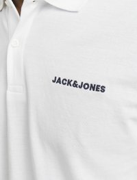 Valkoinen polo-paita, jossa on kaulus, ja rintakarhassa on tummansininen "JACK&JONES" -logo. Valmistettu teksturoidusta puuvillakankaasta.