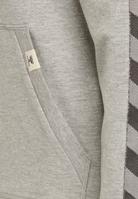 Sudadera gris con un bolsillo lateral, puños acanalados y un patrón texturizado con rayas gris oscuro a lo largo de una manga.