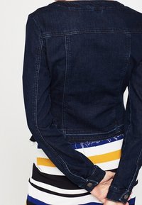 Dark denim jacket with a fitted design, featuring a rounded collar, long sleeves, and buttoned cuffs, paired with a striped dress.