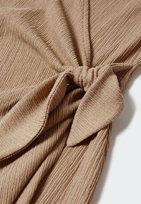 Tissu beige texturé avec un design noué au centre, présentant des lignes côtelées horizontales et une douceur, avec un aspect drapé.