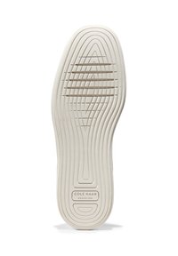 Sole di una scarpa bianca Cole Haan con scanalature curve, linee di battistrada orizzontali e "COLE HAAN GRAND.360" impresso vicino al tallone.