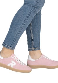 Baskets en suède rose avec des accents blancs, dotées d'une fermeture à lacets blanche et d'une semelle en caoutchouc beige, associées à un jean bleu clair longueur cheville.