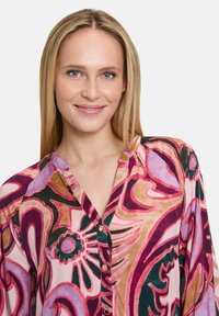 Camicia a maniche lunghe, con bottoni, in un vivace motivo floreale con tonalità di rosa, verde e oro. Tessuto strutturato con colletto e bottoni dorati.