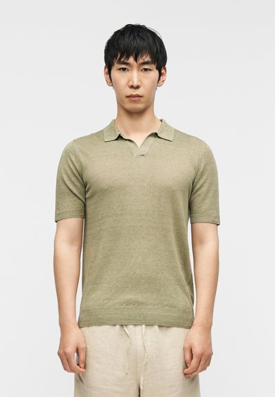 Polo de manga corta en verde claro, con textura de punto, cuello y diseño de escote en v. Se lleva con pantalones de corte relajado y color claro.