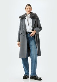 Abrigo de mezcla de lana gris con cuello de piel, diseño de doble botonadura, bolsillos frontales, combinado con unos vaqueros de cintura alta azul claro y zapatos de plataforma negros.