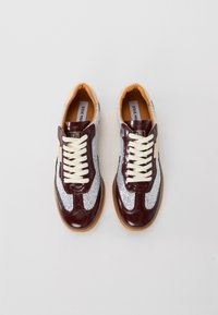 Par nogavic z nizkim profilem iz temno rdeče usnja, srebrnih mrežastih panelov, kremastih vezalk in svetlo rjavih gumijastih podplatov, prikazanih drug ob drugem na beli podlagi.