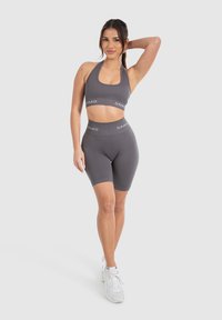 Conjunto atlético gris que incluye un top halter corto y pantalones cortos de cintura alta. La tela es suave con una textura delicada, realzada por una banda con logotipo.