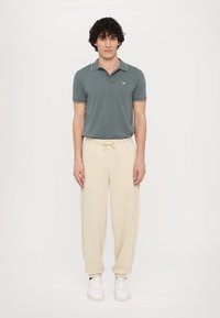Groene polo met witte afwerking, gecombineerd met crème-kleurige, losse joggingbroeken en witte sneakers. Eenvoudig ontwerp, comfortabele pasvorm.