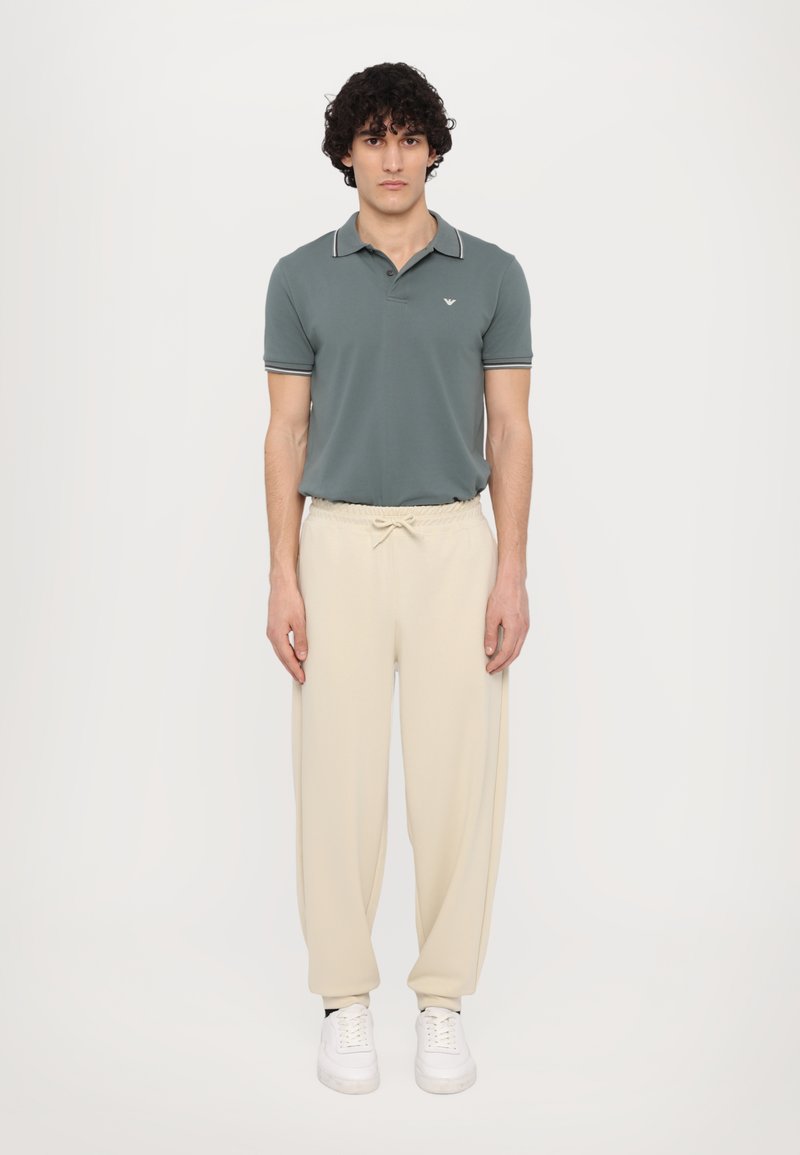 Groene polo met witte afwerking, gecombineerd met crème-kleurige, losse joggingbroeken en witte sneakers. Eenvoudig ontwerp, comfortabele pasvorm.