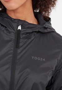 Black lightweight jacket featuring a zip closure, adjustable hood, and TOG24 logo. Smooth texture with a sleek, minimalist design.
