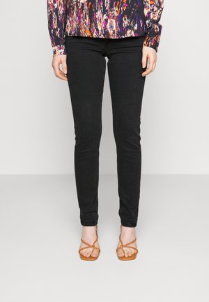 Jeans skinny negros con una textura suave, complementados con una blusa de estampado colorido. El conjunto se acompaña de sandalias marrones de tiras.