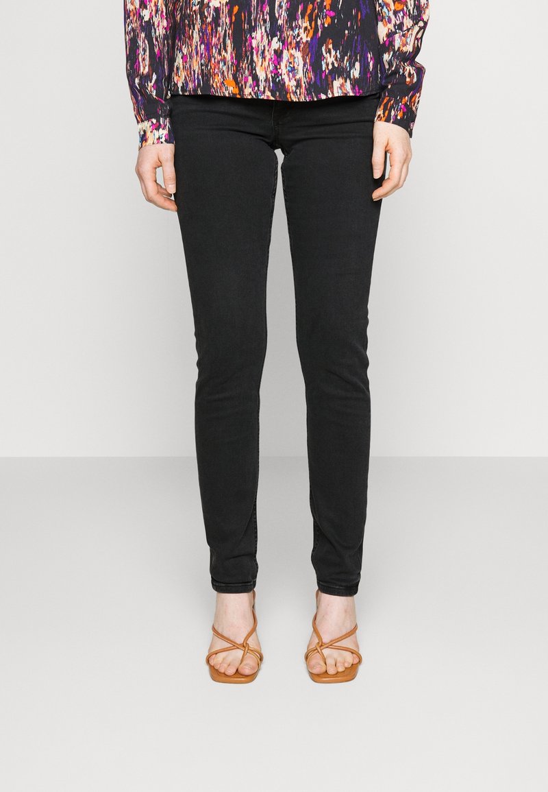 Jeans skinny negros con una textura suave, complementados con una blusa de estampado colorido. El conjunto se acompaña de sandalias marrones de tiras.