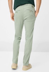 Pantaloni di cotone verde chiaro con design a gamba dritta, due tasche posteriori con bottoni e una texture liscia. Abbinati a scarpe beige.
