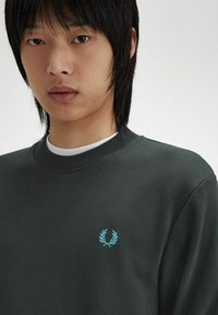 Sudadera de color verde oscuro hecha de una mezcla de algodón, con cuello redondo y cuello acanalado, y un pequeño logotipo bordado en azul claro en el pecho.