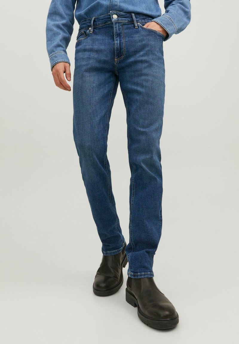 Sötétkék, slim fit farmernadrág, klasszikus öt zsebes kialakítással és enyhe elhalványult textúrával, fekete bokacsizmával párosítva.