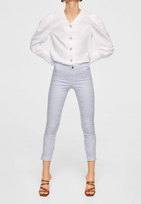 Bílá košile s balónovými rukávy, doplněná modro-bílými pruhovanými úzkými kalhotami a hnědými sandály na pásku.