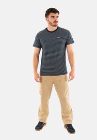T-shirt à rayures bleu marine et blanches avec un col rond, associé à un chino beige et des baskets noires avec des accents marron.