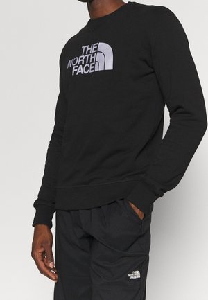 Sweatshirt en coton noir avec un logo argenté sur la poitrine, poignets et ourlet côtelés. Associé à un pantalon noir, offrant une coupe décontractée.