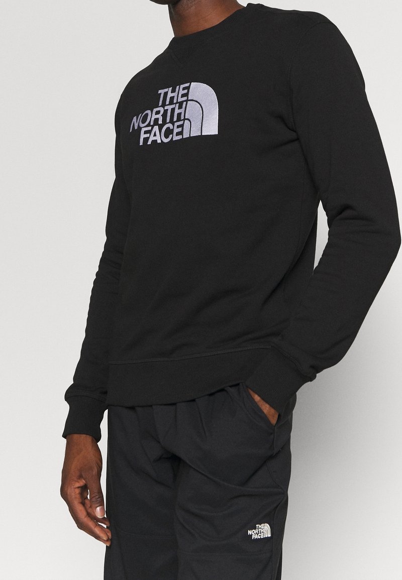 Svart bomullströja med en silverfärgad logotyp på bröstet, ribbade ärmslut och nederkant. Kombineras med svarta byxor som ger en avslappnad passform.