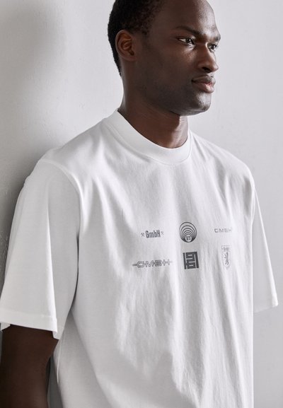 Weißes Baumwoll-T-Shirt mit verschiedenen grauen Grafiken. Klassischer Rundhalsausschnitt, kurze Ärmel und eine lockere Passform.