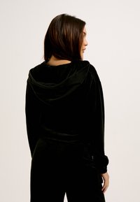 Hoodie de veludo preto com capuz ajustável, mangas longas e um corte descontraído. Apresenta uma textura suave e um design simples.