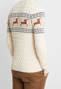 Kremowy sweter w splot kablowy z wzorzystą yoke z reniferami i geometrycznymi wzorami w odcieniach brązu i granatu. Ribbowane mankiety i dół.