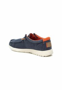 Zapato de lona azul marino con suela beige, acentos naranjas y diseño sin cordones. Presenta una textura suave y un estilo minimalista, adecuado para uso casual.