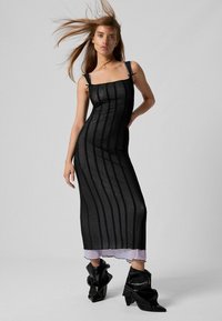 Čierne pruhované šaty s tenkými ramienkami, textúrovaná tkanina, priliehavý strih, prekryté svetlofialovým spodným šatom, doplnené čiernymi čižmami.