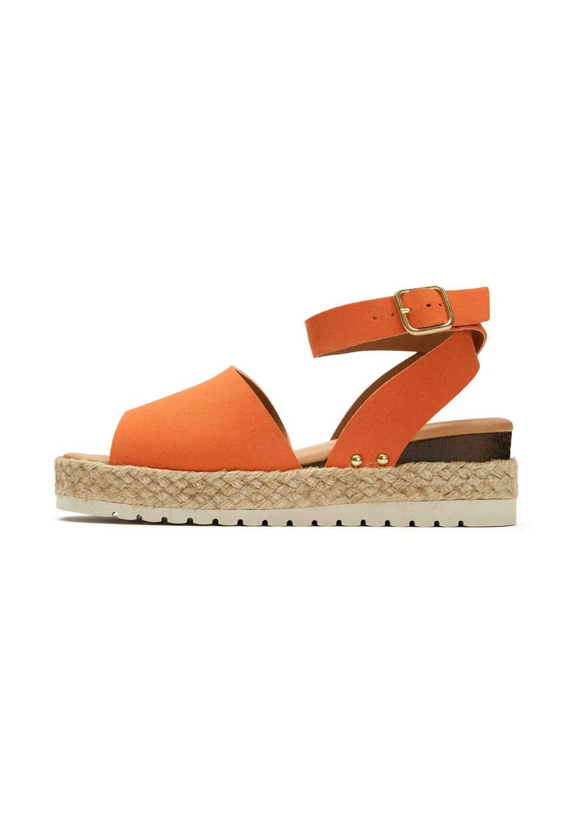 Orange suede sandal with a wide toe strap and ankle strap. Features a woven jute midsole and a flat white rubber sole. Gold buckle detail.