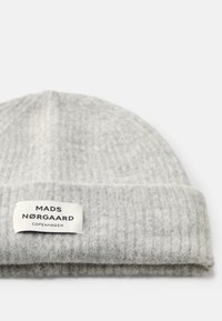 Beanie grigio lavorato a maglia con una texture a costine. Presenta un'etichetta bianca con la scritta "MADS NØRGAARD COPENHAGEN" stampata in nero. Design semplice.