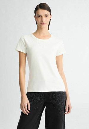 T-shirt en coton blanc à manches courtes, col rond et détails de perles décoratives le long de l'empiècement. Associé à un jean noir avec des accents de clous.