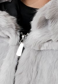 Chaqueta de piel sintética gris con una textura suave, que presenta una cremallera plateada y un diseño elegante. Los detalles incluyen un tirador de cremallera brillante.