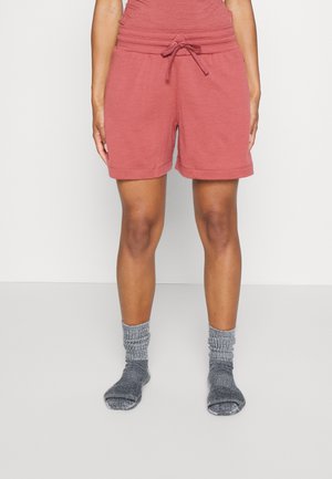Personne portant un short corail à cordon et des chaussettes grises, debout devant un fond clair uni.