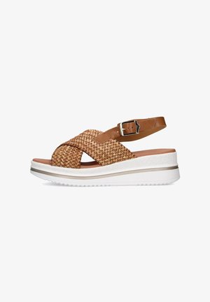 Sandal in paglia intrecciata e pelle marrone con cinturini incrociati, fibbia alla caviglia regolabile e suola piatta bianca con un sottile accento beige.