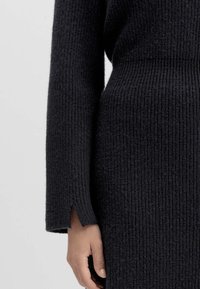 Dunkelrippstrick- Kleidungsstück mit langen Ärmeln, das einen Schlitz am Bündchen aufweist. Die Textur ist dick und weich und vermittelt ein gemütliches Aussehen.