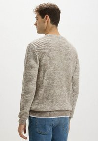 Maglione a coste di colore marrone chiaro con scollatura rotonda e maniche lunghe, caratterizzato da un tessuto testurizzato e una vestibilità comoda, indossato sopra jeans blu.