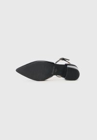 Scarpa nera a punta con finitura lucida, caratterizzata da un sottile cinturino alla caviglia e un tacco basso a blocco. Suola in gomma testurizzata.