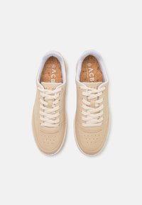 Beige sneakers with a smooth suede upper, white laces, and perforated detailing on the toe box. Cork insole with branding visible.