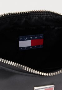 Fekete cipzáras belső zseb, textil címkével, amelyen a "TOMMY JEANS" felirat és egy piros, fehér, kék négyszögletes logó látható. Simább textúra.