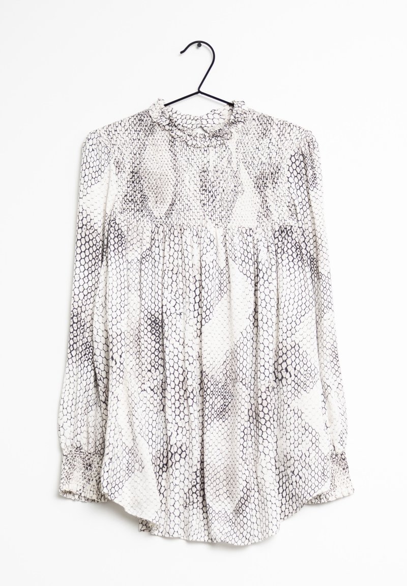 Blouse blanche à manches longues avec motif en faux serpent hexagonal noir, col montant à volants et poignets froncés, accrochée à un cintre noir.