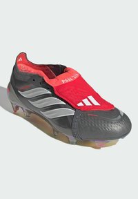 Sort og rød fodboldstøvle med syntetisk overdel, tekstureret finish, markante sølvstriber og slip-on design med synlige knopper.