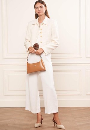 Veste blanche texturée avec des boutons dorés, associée à un haut blanc et un pantalon large. Sac à main beige de forme incurvée avec une poignée courte. Talons aiguilles beiges.