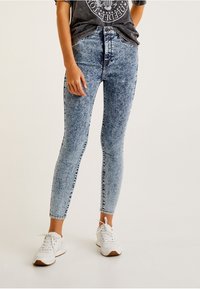 Jeans ajustados de mezclilla color azul claro con un patrón desgastado y descolorido. Diseño de cintura alta combinado con una camiseta gráfica relajada y zapatillas blancas.