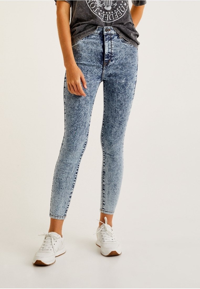 Jeans ajustados de mezclilla color azul claro con un patrón desgastado y descolorido. Diseño de cintura alta combinado con una camiseta gráfica relajada y zapatillas blancas.